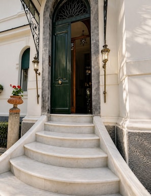 A set of marble stairs leading to a green door with a decorative arch above it. - Casa Rubinacci (Napoli)
