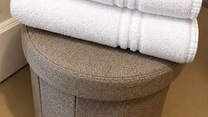 A stack of white towels and a pair of white slippers on a textured stool. - Casa Rubinacci (Napoli)