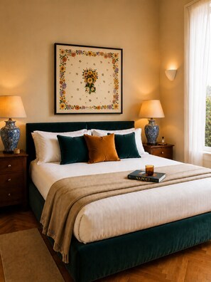 A neatly made bed with a green headboard, two bedside lamps, a framed floral artwork, and a book on the bed.