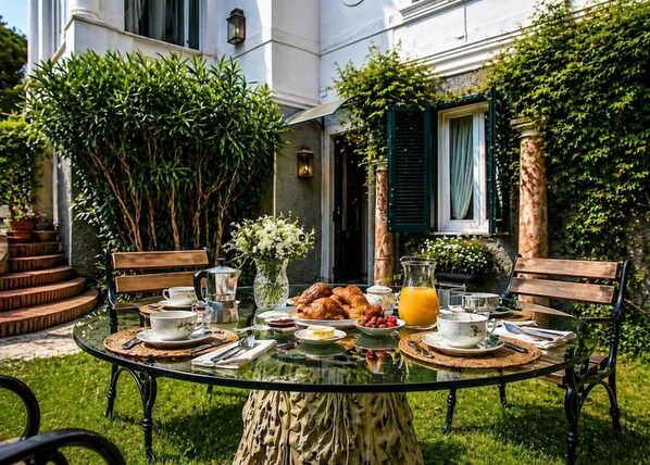 An outdoor dining area with a glass table, chairs, and a variety of breakfast items.