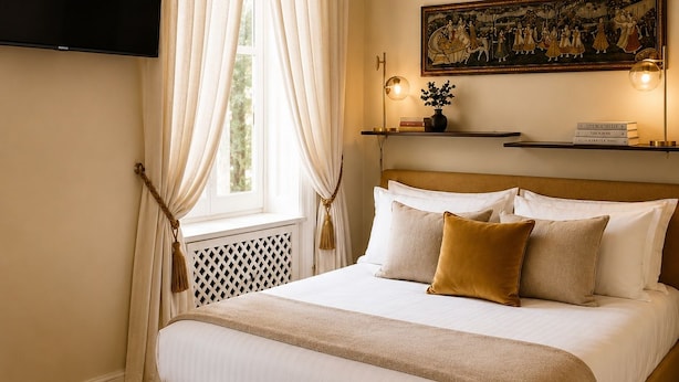 A hotel room with a bed, curtains, a painting, a shelf with books, and a television. - Casa Rubinacci (Napoli)