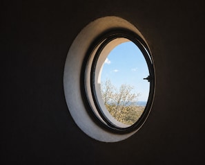 Una ventana redonda con vista a árboles y un cielo despejado.