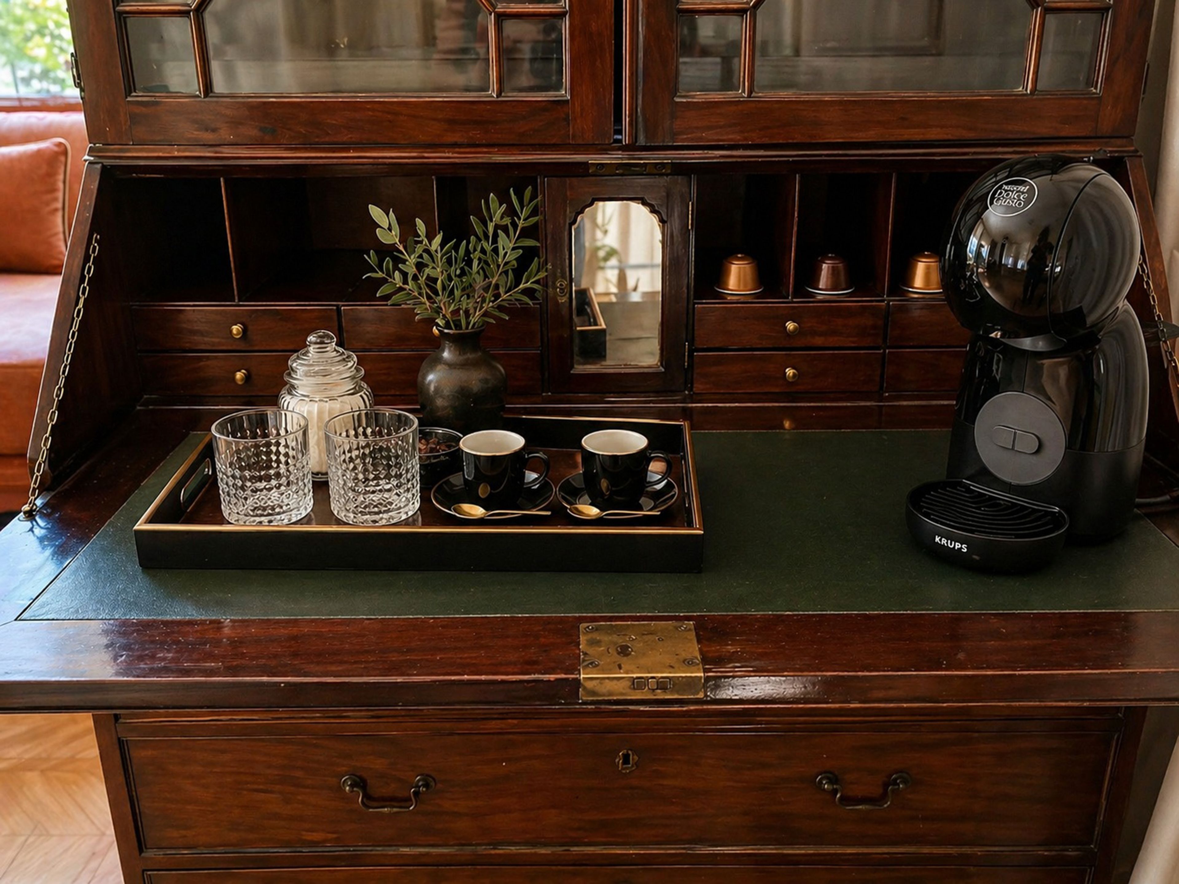 A wooden desk with a tray holding glasses, a vase with greenery, and a coffee maker.