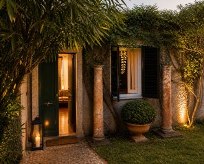 A well-lit entrance with a green door, a window with black shutters, and a stone pillar.