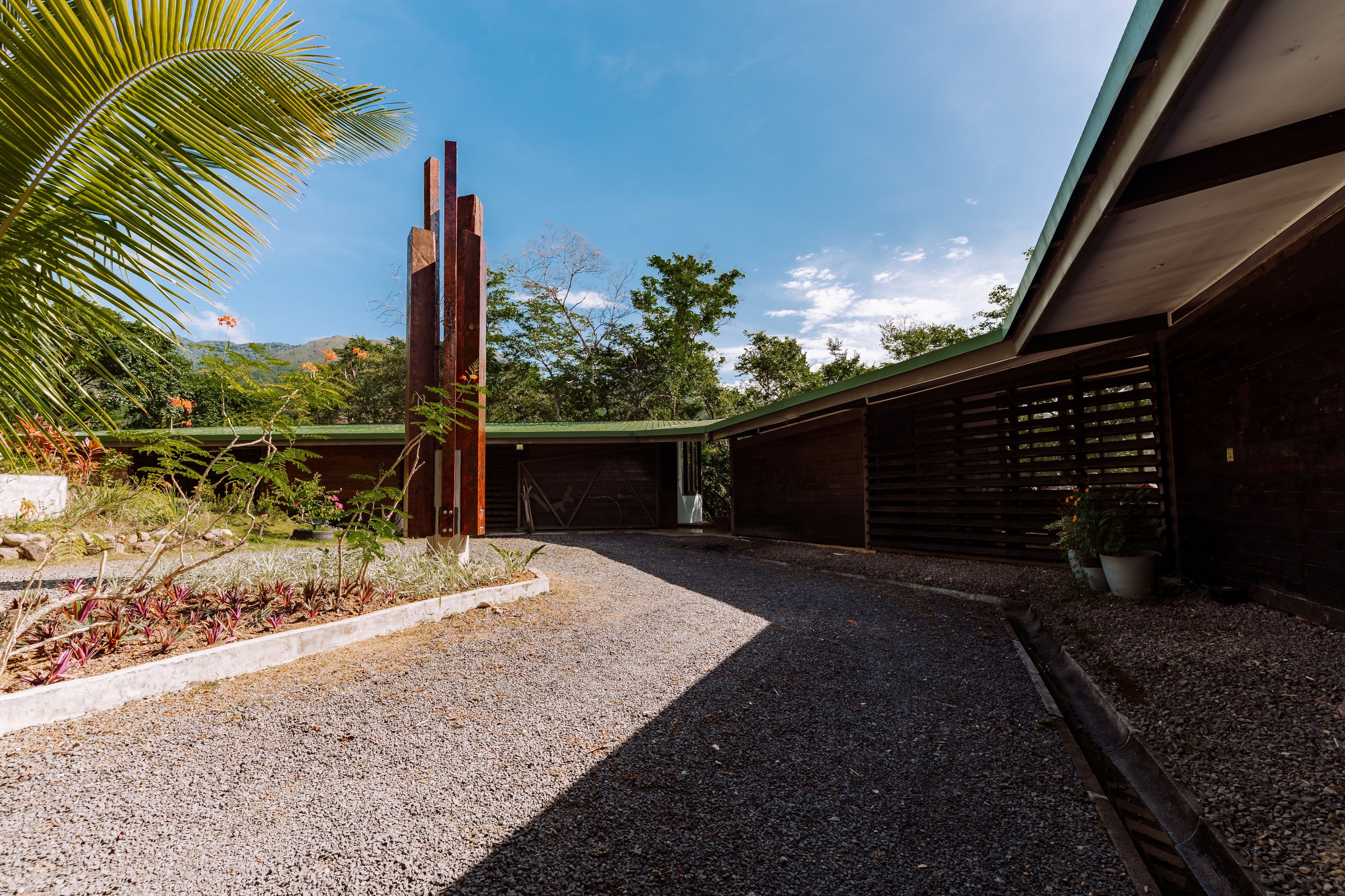 A gravel pathway leading to a building with a green roof, surrounded by greenery and a clear sky.