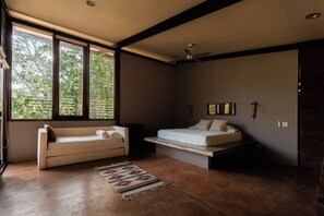 Un dormitorio moderno con sofá, cama, ventilador de techo y ventanas amplias.