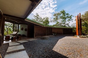 Un espacio exterior moderno con un sendero de grava, escalones de madera y una zona de estar cubierta.
