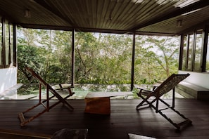 Un terrazzo in legno con due sedie e un tavolo, con vista su un paesaggio verdeggiante.