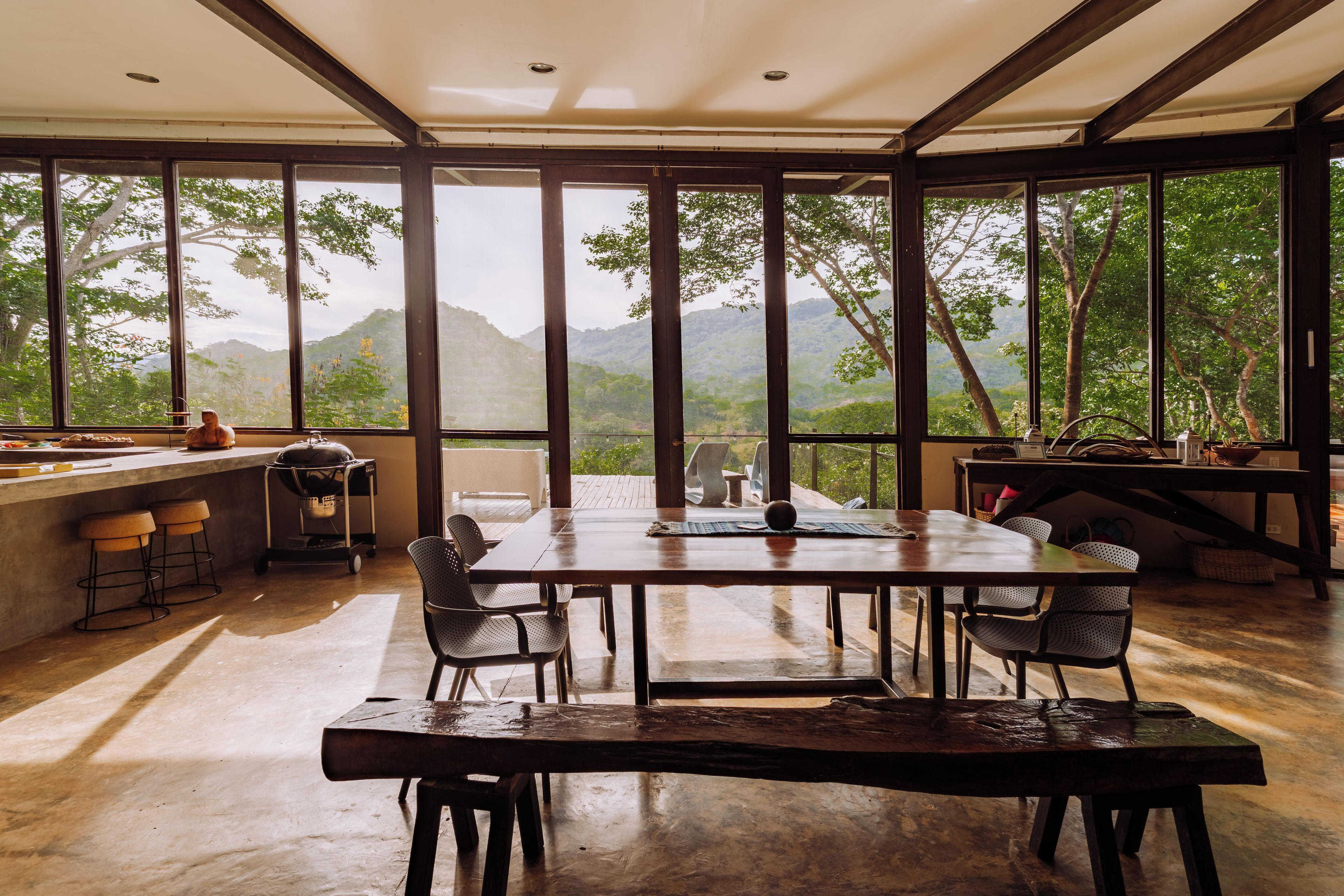 A spacious dining area with a large table and chairs, large windows offering a view of a mountainous landscape.