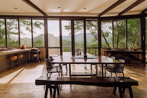A spacious dining area with a large table and chairs, large windows offering a view of a mountainous landscape.