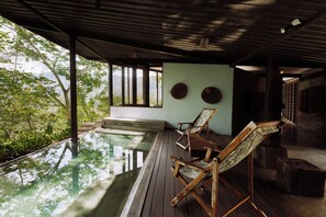 Ein Infinity-Pool mit Holzliegen, Blick auf Grünflächen und eine schlichte Wand mit zwei runden Dekorationen.