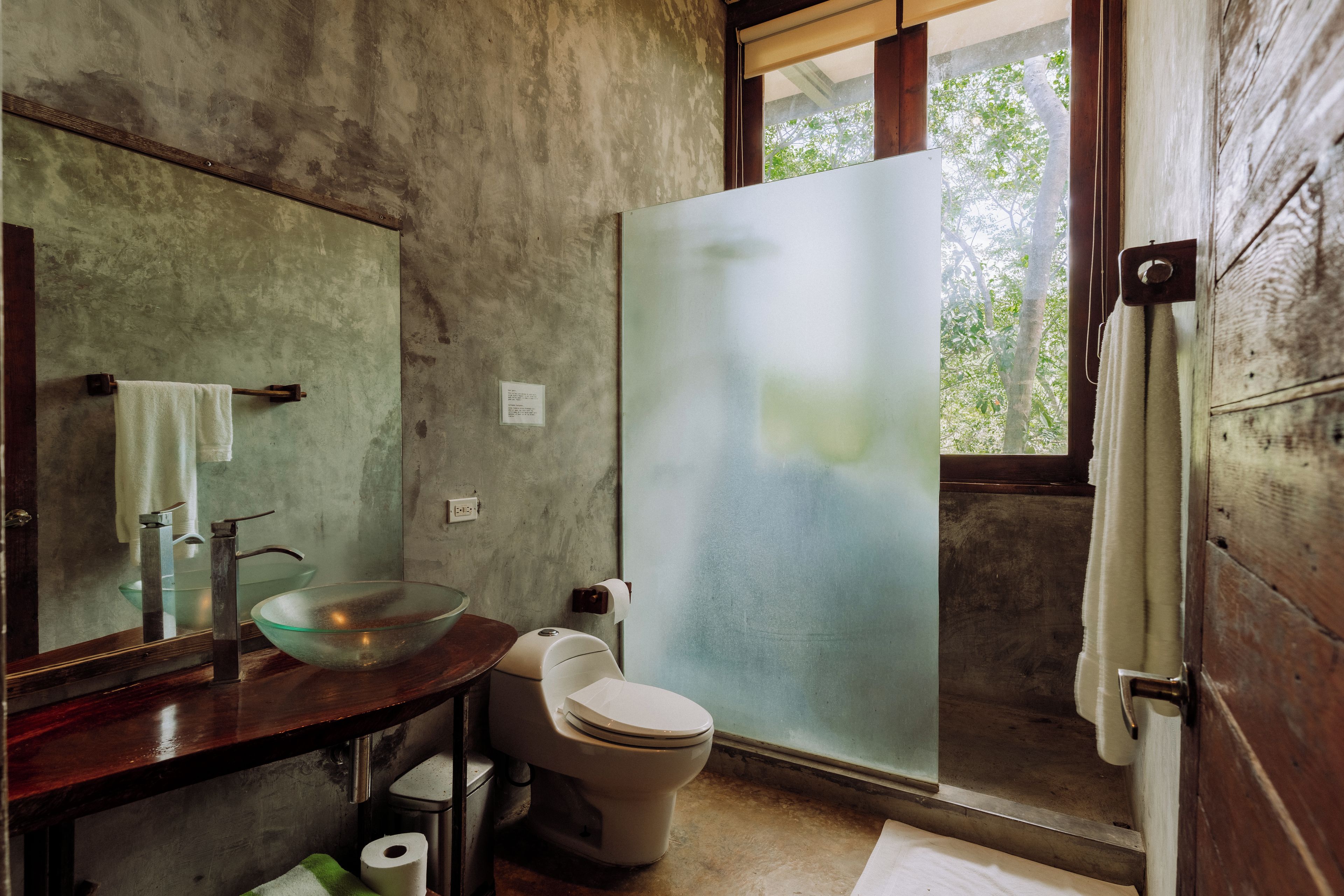 A bathroom with a large mirror, a glass bowl sink, a toilet, and a frosted glass shower door.