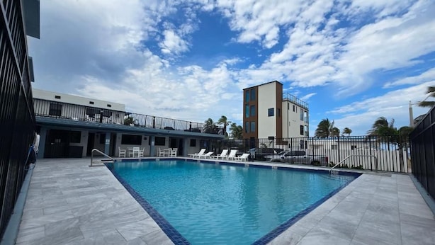 A swimming pool with a tiled deck, lounge chairs, and a building in the background. - Free Parking Beach Condo - Beach Terrace (Hollywood)