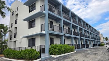 A multi-story hotel with balconies, a parking area, and a clear sky.
