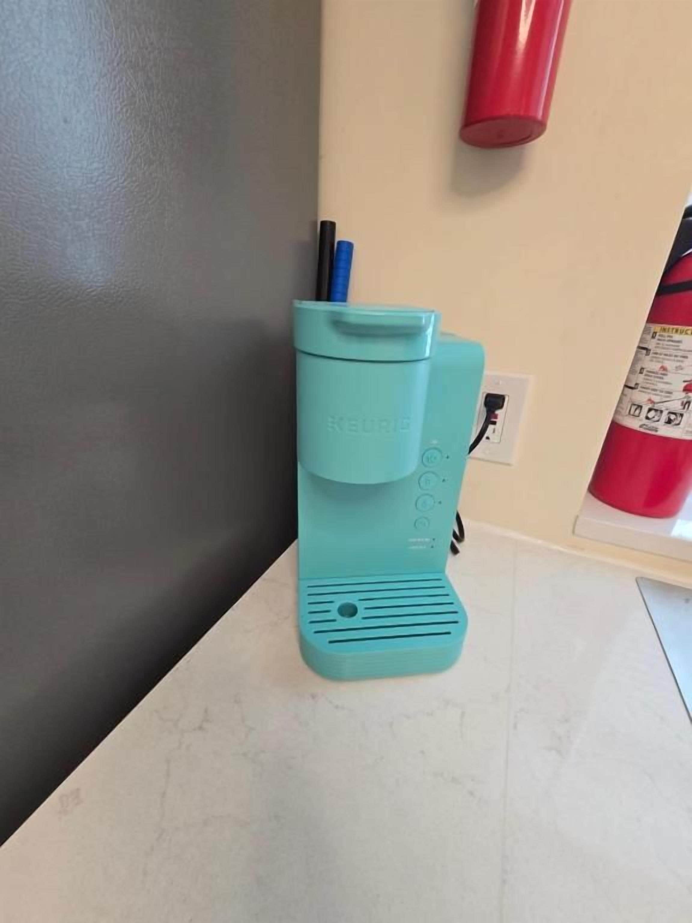 A teal-colored coffee maker with a power cord on a white countertop.