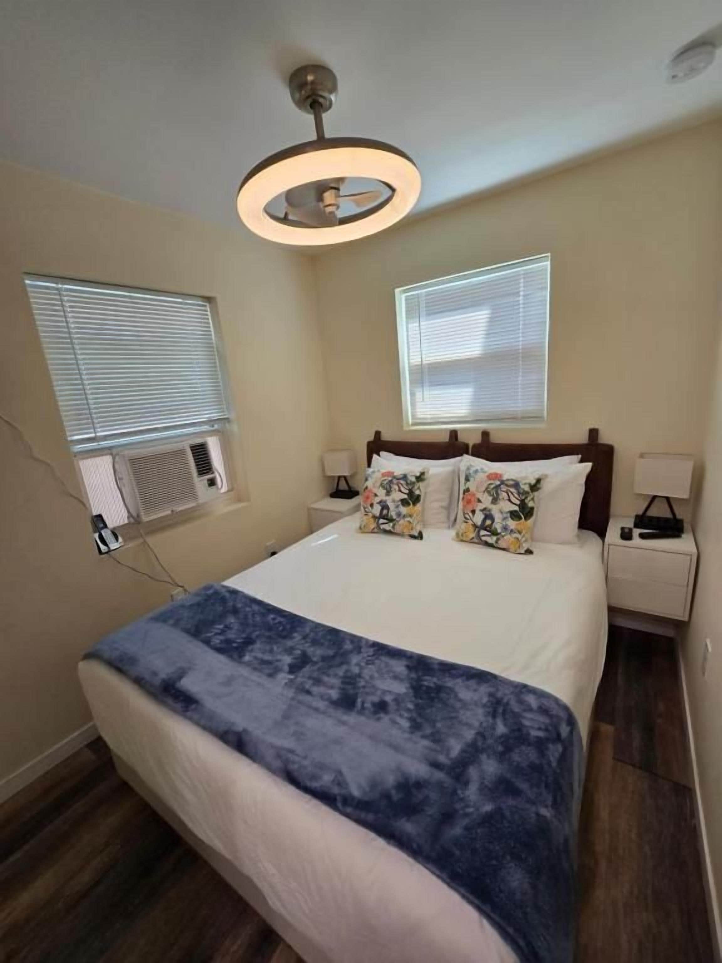 A bedroom with a bed, bedside tables, a ceiling fan, and windows.