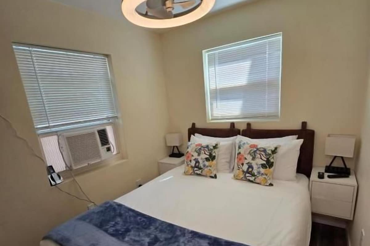 Ein Schlafzimmer mit einem Bett, Nachttischen, einem Deckenventilator und Fenstern.