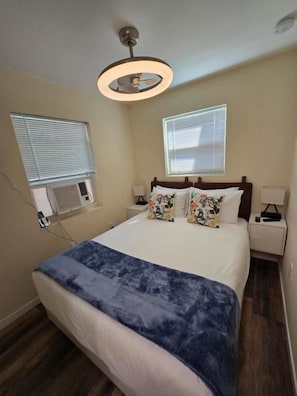 Ein Schlafzimmer mit einem Bett, Nachttischen, einem Deckenventilator und Fenstern.