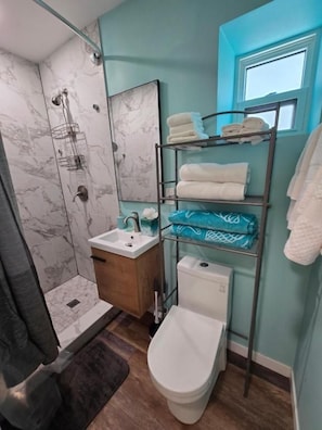 Ein Badezimmer mit Dusche, Toilette, Waschbecken und einem Handtuchhalter mit Handtüchern.
