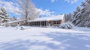 Ein Haus mit überdachter Veranda, einem mit Schnee bedeckten Rasen und Bäumen.