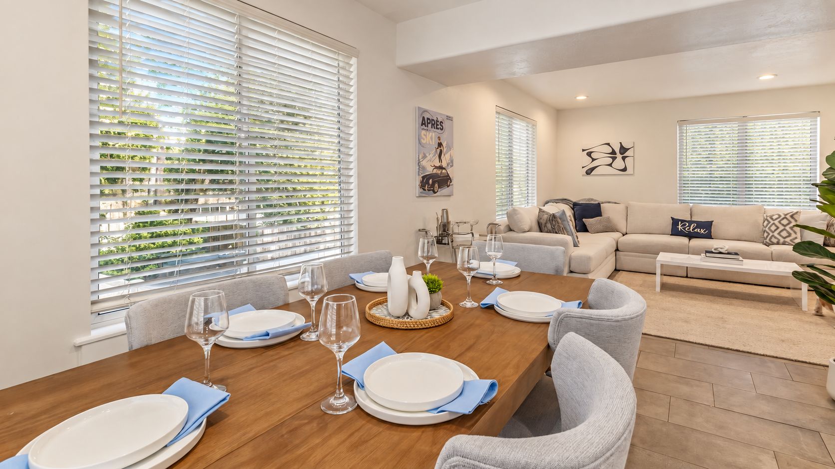 A dining area with a wooden table set for six, surrounded by grey chairs.