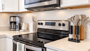 A modern kitchen with a stainless steel stove, a coffee maker, and a set of knives in a wooden holder. - 3BR Modern Retreat | Hot Tub | Near 4 Ski Resorts (South Salt Lake)