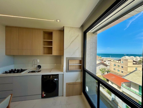 A modern kitchen with built-in appliances and a large window offering a view of the sea.