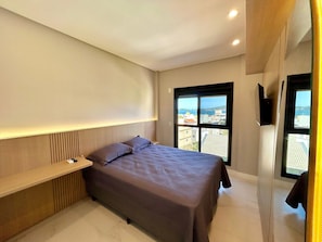 A modern bedroom with a bed, bedside table, and a large window offering a city view. - Mirante do Oceano Hospedaria (Bombinhas)