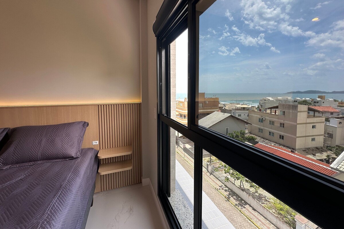 A bedroom with a large window, a bed, and a built-in shelf.