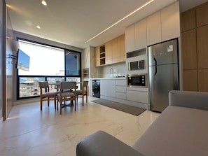 A modern kitchen with built-in appliances, a dining area with chairs, and a large window offering a city view.