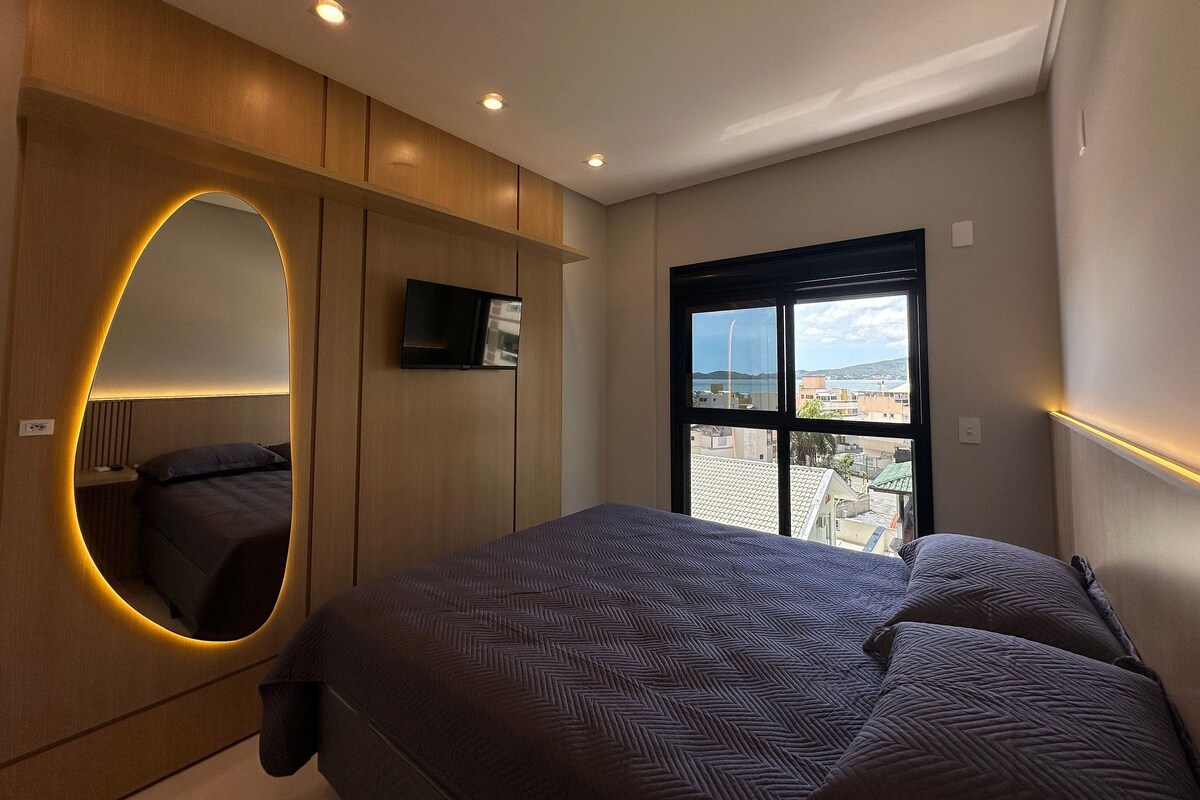 A modern bedroom with a bed, a TV, and a large window with a city view.