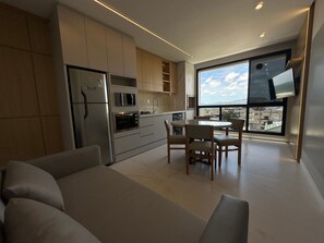A modern kitchen with built-in appliances, a dining area with a round table, and a large window offering a city view.