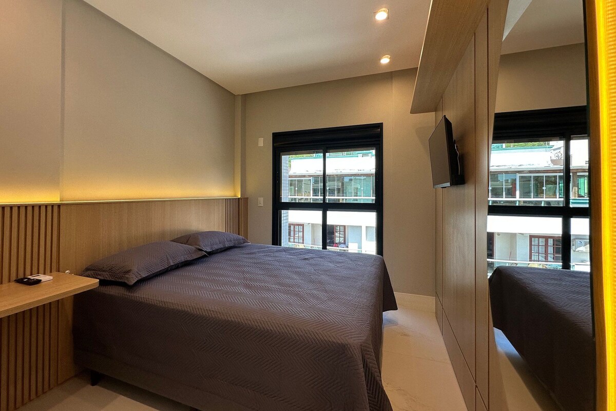 A modern bedroom with a bed, bedside table, and a large window.