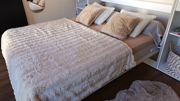 Een bed met een zachte witte deken en kussens, een nachtkastje met een lamp, en een houten vloer.