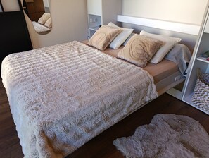 Un lit recouvert d’une couverture blanche et moelleuse, avec des oreillers, une table de chevet dotée d’une lampe et un plancher en bois.