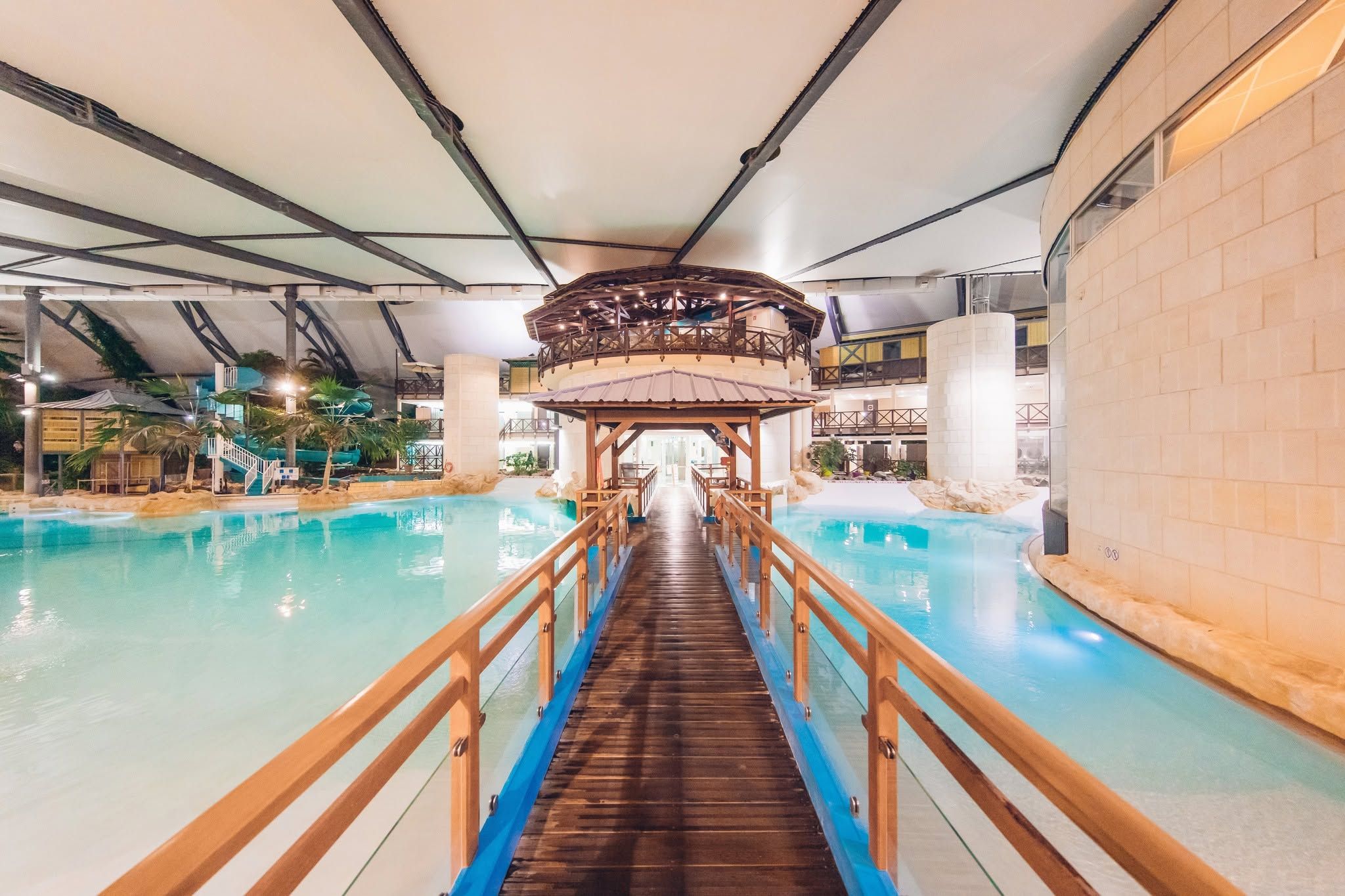 An indoor swimming pool with a wooden walkway leading to a covered area.