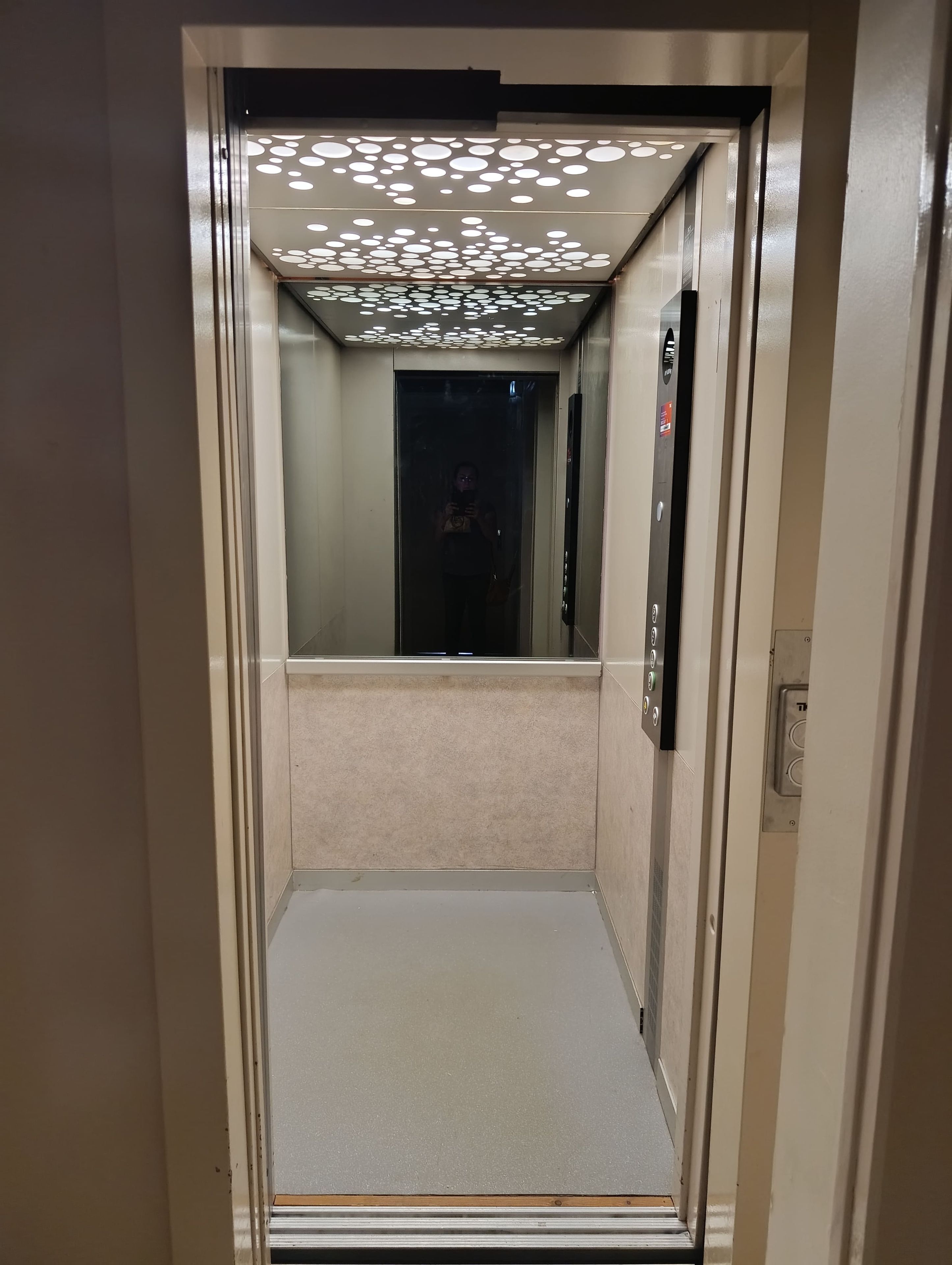 L’intérieur d’un ascenseur, avec un plafond réfléchissant et un panneau de commande situé à droite.
