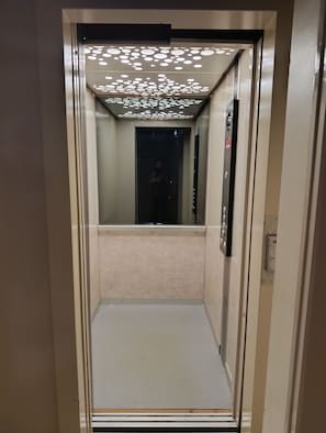 Un ascenseur doté d’un intérieur réfléchissant et d’un plafond orné de motifs.