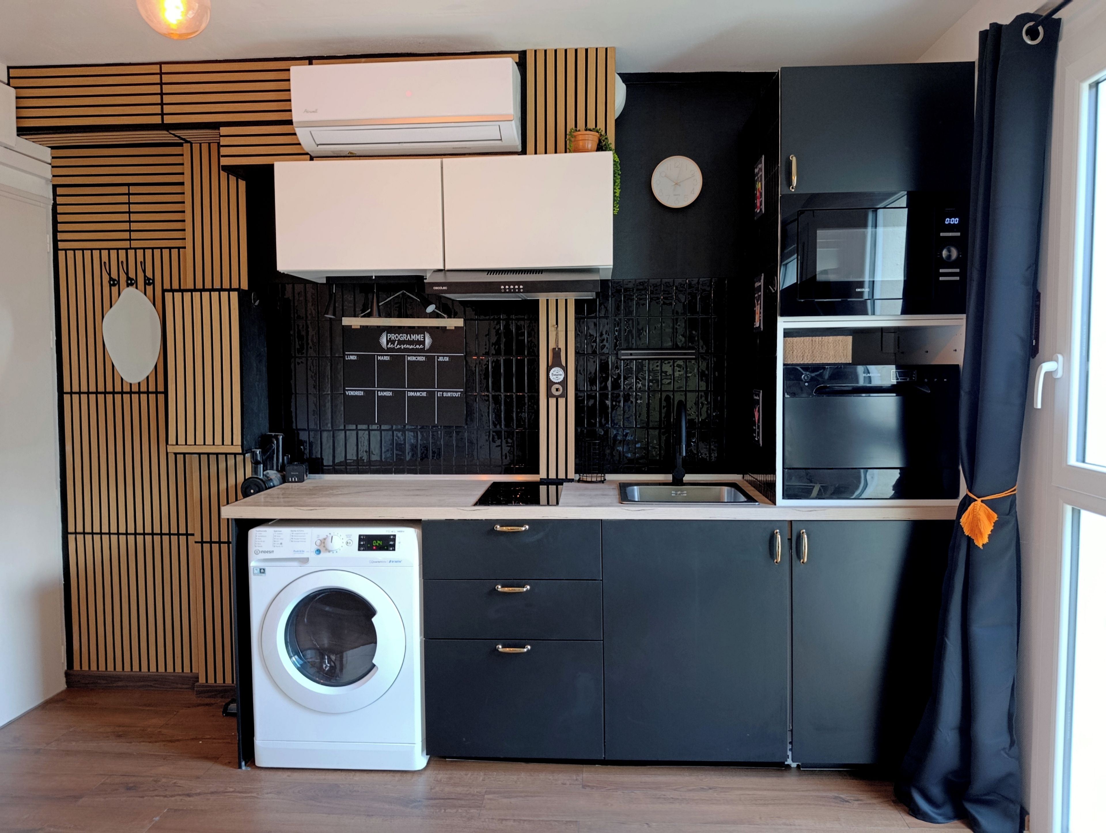 Een compacte keuken met een wasmachine, een magnetron en een zwarte oven.