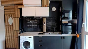 Een compacte keuken met een wasmachine, een magnetron en een zwarte oven.