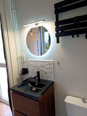 A bathroom with a black sink, a round mirror, and a white toilet. - Vrbo Property (Jonzac)