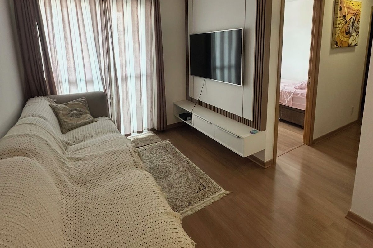 Un dormitorio moderno con una cama grande, un televisor montado en la pared y una puerta que da a otra habitación.