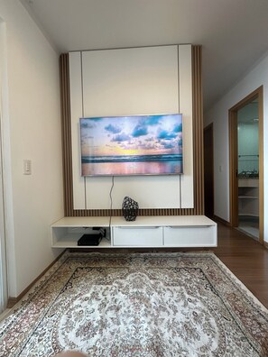 Una sala moderna con un televisor de pantalla plana montado en la pared, un adorno mural y un tapete estampado en el suelo.