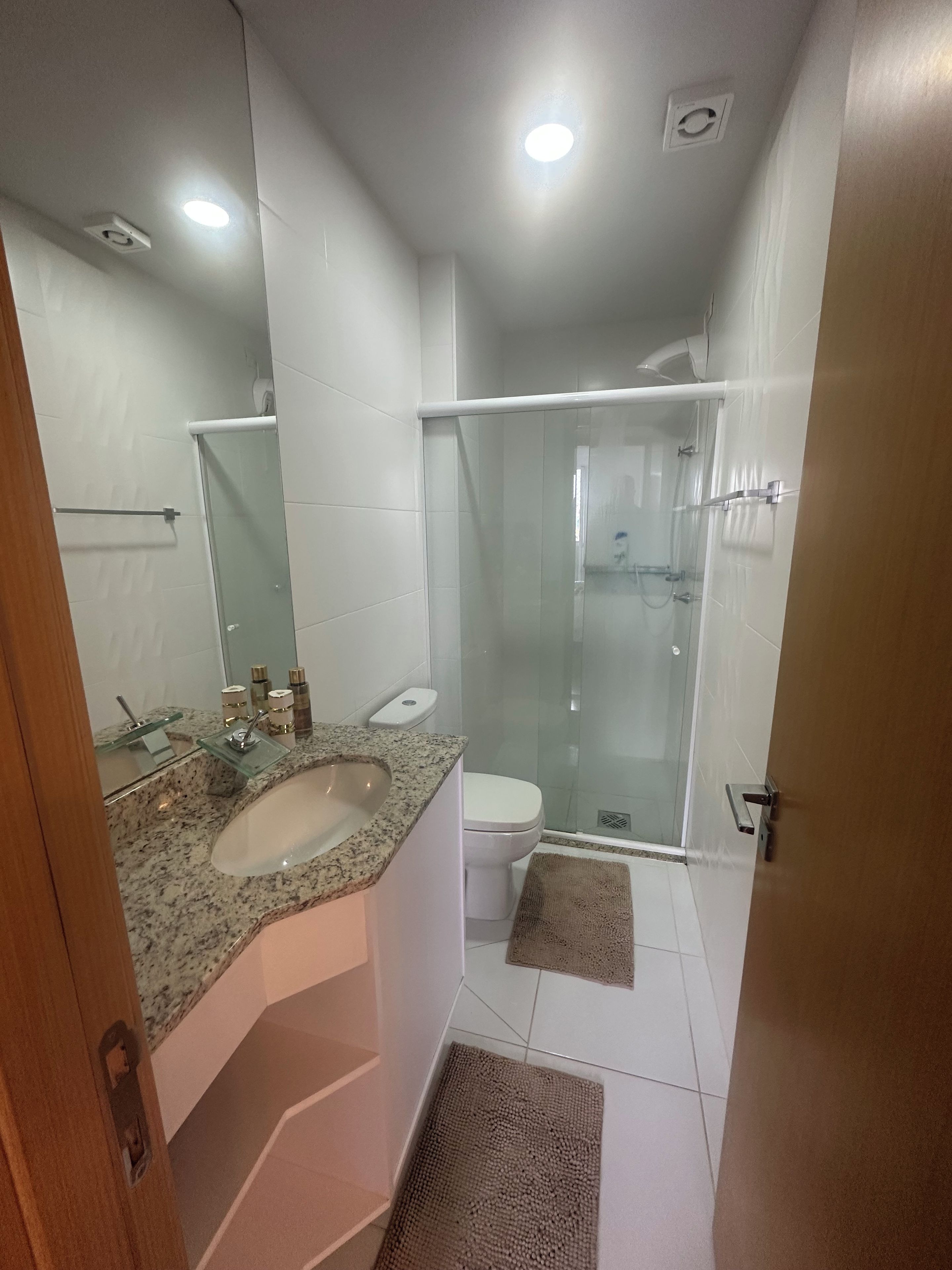 A bathroom with a glass shower enclosure, a sink with a granite countertop, and a toilet.