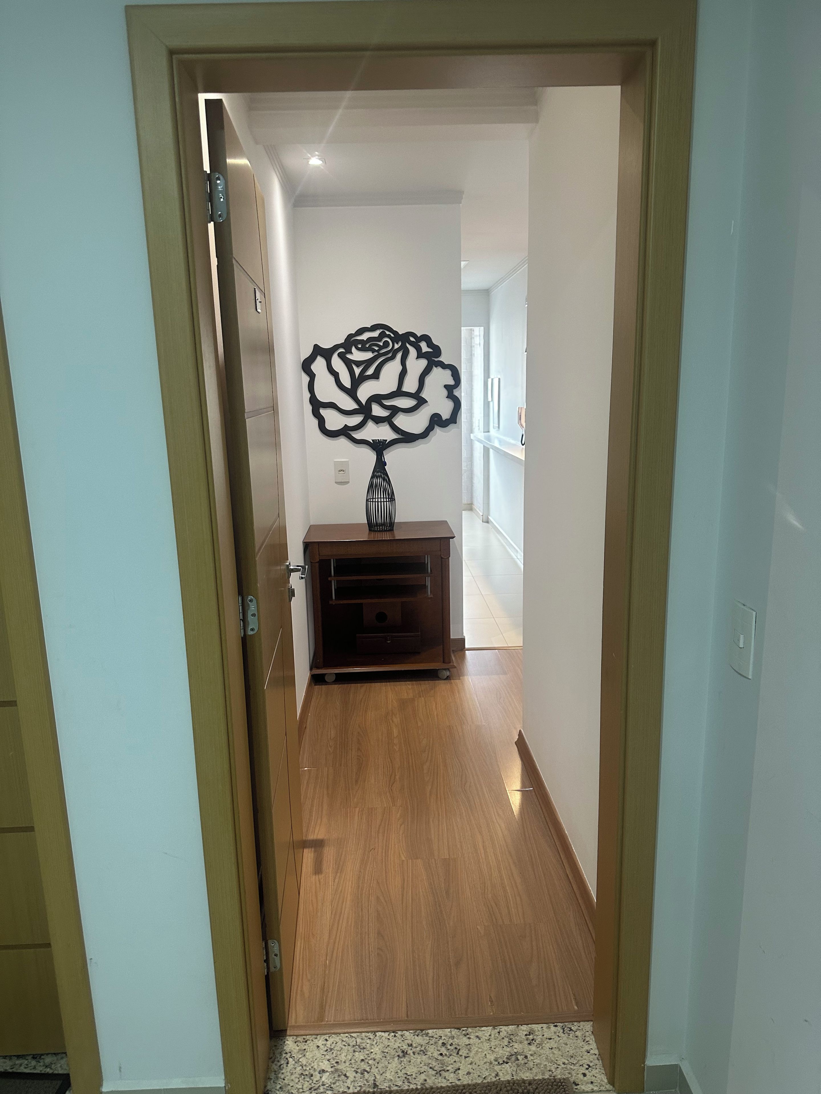 Un couloir doté d’un plancher en bois, d’un élément décoratif fixé au mur et d’une petite armoire en bois.