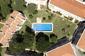 An aerial view of a residential area with a swimming pool, surrounded by greenery and adjacent to a building with a tiled roof. - Apartment 'Vilamoura Garden View' with Shared Pool, Wi-Fi and Air Conditioning (Quarteira)