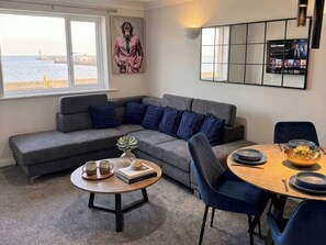 A modern living room with a grey sofa, a round wooden table, and a view of the sea through large windows. - Sea View Luxury Apartment Sleeps 5 - Fast Wifi - off Street Parking - Contractors Dream (Sheerness)