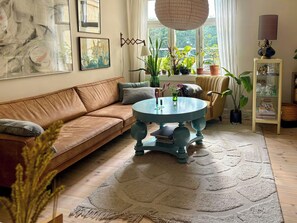 Uma sala de estar aconchegante com um sofá de couro marrom, uma mesa redonda azul e diversas plantas em vasos.