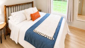 Een slaapkamer met een bed, een plafondventilator, een raam met gordijnen, een nachtkastje en een aan de muur hangend schilderij.