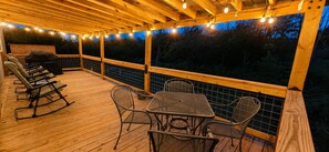 Um deck externo com piso de madeira, cadeiras de metal, uma mesa e luzes de corda.